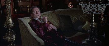 Movie still from “The Skull” (1965), directed by Freddie Francis – An older man sitting on top of a couch; Medium shot, High angle