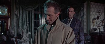 Movie still from “The Skull” (1965), directed by Freddie Francis – A man in a trench coat standing next to another man in a tie; Medium shot, Over the shoulder angle