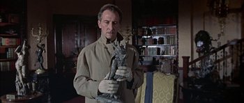 Movie still from “The Skull” (1965), directed by Freddie Francis – A man in a tan jacket holding a statue; Medium shot, Low angle