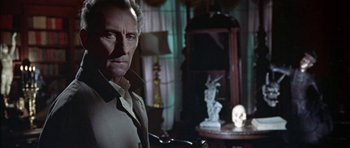 Movie still from “The Skull” (1965), directed by Freddie Francis – A person in a room near a table; Medium shot, Over the shoulder angle