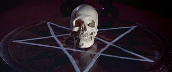 Movie still from “The Skull” (1965), directed by Freddie Francis – A skull sitting on top of a wooden table in front of a pentagram; Extreme Close Up shot, Overhead angle