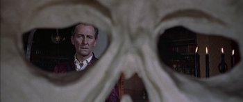 Movie still from “The Skull” (1965), directed by Freddie Francis – A man standing in front of a skull looking at the camera; Close Up shot, Over the shoulder angle