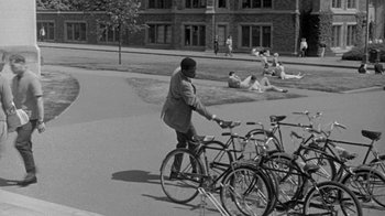 Movie still from “The Slender Thread” (1965), directed by Sydney Pollack – A man riding a bike down a street next to parked bicycles; Wide shot, High angle
