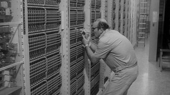 Movie still from “The Slender Thread” (1965), directed by Sydney Pollack – An old photo of a man working on a computer; Medium shot, Low angle