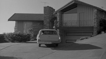 Movie still from “The Slender Thread” (1965), directed by Sydney Pollack – An old car parked in front of a brick house; Wide shot, Low angle