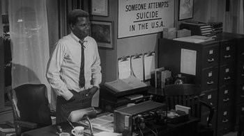Movie still from “The Slender Thread” (1965), directed by Sydney Pollack – A black and white photo of a man standing in front of a desk; Medium shot, Low angle