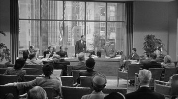 Movie still from “The Solid Gold Cadillac” (1956), directed by Richard Quine – A group of people sitting in a room with chairs; Wide shot, High angle