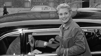 Movie still from “The Solid Gold Cadillac” (1956), directed by Richard Quine – A young woman is smiling in the driver's seat of a car; Medium shot, Over the shoulder angle