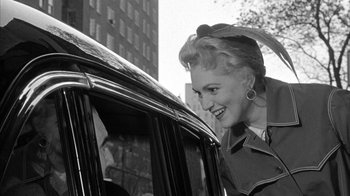 Movie still from “The Solid Gold Cadillac” (1956), directed by Richard Quine – An old black and white photo of a woman standing next to a car; Close Up shot, Over the shoulder angle