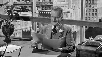 Movie still from “The Solid Gold Cadillac” (1956), directed by Richard Quine – An older man sitting at a desk with papers in front of him; Medium shot, Over the shoulder angle