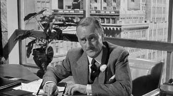 Movie still from “The Solid Gold Cadillac” (1956), directed by Richard Quine – An old photo of a man sitting at a table; Close Up shot, Low angle