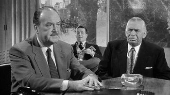 Movie still from “The Solid Gold Cadillac” (1956), directed by Richard Quine – A group of men sitting at a table in front of a window; Medium shot, Over the shoulder angle