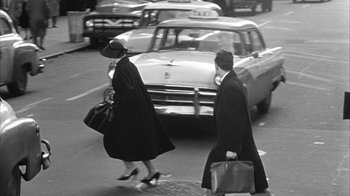 Movie still from “The Solid Gold Cadillac” (1956), directed by Richard Quine – A man and a woman crossing a street in front of a car; Wide shot, Low angle