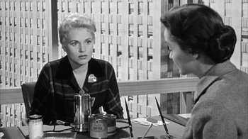 Movie still from “The Solid Gold Cadillac” (1956), directed by Richard Quine – A woman sitting at a table in front of another woman; Medium shot, Over the shoulder angle