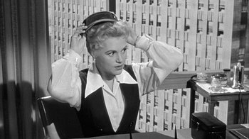 Movie still from “The Solid Gold Cadillac” (1956), directed by Richard Quine – An old photo of a woman putting on a hat; Medium shot, Low angle