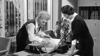 Movie still from “The Solid Gold Cadillac” (1956), directed by Richard Quine – Two women working together on a piece of paper in an office setting; Medium shot, Low angle