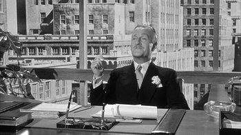Movie still from “The Solid Gold Cadillac” (1956), directed by Richard Quine – A man in a suit sitting at a table; Medium shot, Low angle