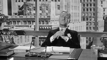 Movie still from “The Solid Gold Cadillac” (1956), directed by Richard Quine – An old photo of a man sitting at a desk; Medium shot, Low angle
