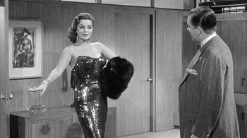 Movie still from “The Solid Gold Cadillac” (1956), directed by Richard Quine – A woman in a sequined dress holding onto a fur bag; Medium shot, Over the shoulder angle