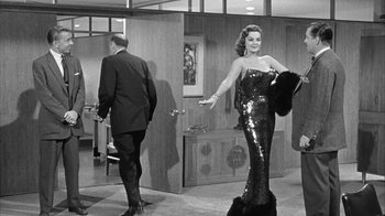 Movie still from “The Solid Gold Cadillac” (1956), directed by Richard Quine – An old photo of a man and a woman in a room; Medium shot, Low angle