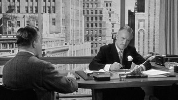 Movie still from “The Solid Gold Cadillac” (1956), directed by Richard Quine – A man sitting at a table in front of another man; Medium shot, Over the shoulder angle