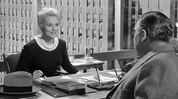 Movie still from “The Solid Gold Cadillac” (1956), directed by Richard Quine – An older woman sitting at a table talking to an older man; Medium shot, Over the shoulder angle