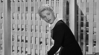 Movie still from “The Solid Gold Cadillac” (1956), directed by Richard Quine – An old black and white photo of a woman leaning against a wall; Medium shot, Low angle