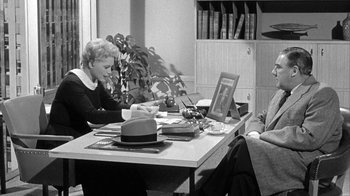 Movie still from “The Solid Gold Cadillac” (1956), directed by Richard Quine – Two people sitting at a table looking at a laptop computer; Medium shot, Over the shoulder angle