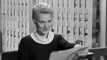 Movie still from “The Solid Gold Cadillac” (1956), directed by Richard Quine – An old photo of a woman in a black and white photo; Medium shot, Over the shoulder angle
