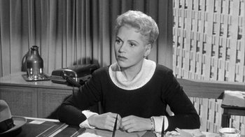 Movie still from “The Solid Gold Cadillac” (1956), directed by Richard Quine – An old black and white photo of a woman sitting at a desk; Medium shot, Over the shoulder angle