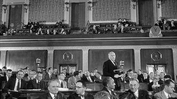 Movie still from “The Solid Gold Cadillac” (1956), directed by Richard Quine – An old photo of a man giving a speech in front of an audience; Wide shot, Low angle