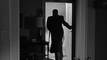 Movie still from “The Solid Gold Cadillac” (1956), directed by Richard Quine – A man in a long black coat walking into a room; Wide shot, Over the shoulder angle