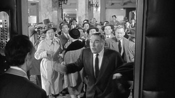 Movie still from “The Solid Gold Cadillac” (1956), directed by Richard Quine – A group of men in suits and hats in front of a crowd; Wide shot, High angle