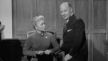 Movie still from “The Solid Gold Cadillac” (1956), directed by Richard Quine – An old photo of a man and a woman in a courtroom; Medium shot, Over the shoulder angle