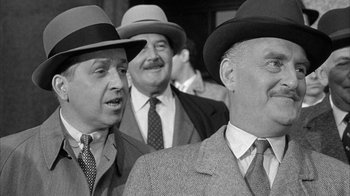 Movie still from “The Solid Gold Cadillac” (1956), directed by Richard Quine – A black and white photo of men in suits and hats; Close Up shot, Over the shoulder angle