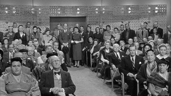 Movie still from “The Solid Gold Cadillac” (1956), directed by Richard Quine – A group of people sitting and standing in a room; Wide shot, High angle
