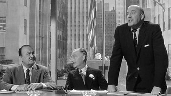 Movie still from “The Solid Gold Cadillac” (1956), directed by Richard Quine – A group of men sitting at a table in front of a building; Medium shot, Over the shoulder angle
