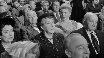 Movie still from “The Solid Gold Cadillac” (1956), directed by Richard Quine – A group of people sitting in a room; Medium shot, Over the shoulder angle