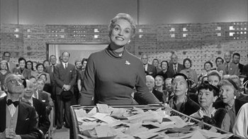 Movie still from “The Solid Gold Cadillac” (1956), directed by Richard Quine – A woman standing in front of a pile of papers; Medium shot, Low angle