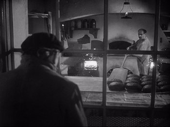 Movie still from “The Song of Bernadette” (1943), directed by Henry King – A man standing in front of an oven in a kitchen; Medium shot, Over the shoulder angle