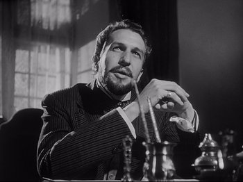 Movie still from “The Song of Bernadette” (1943), directed by Henry King – A black and white photo of a man sitting at a table; Close Up shot, Low angle
