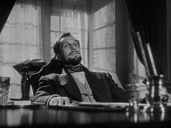 Movie still from “The Song of Bernadette” (1943), directed by Henry King – A man sitting at a desk with a microphone; Medium shot, Low angle