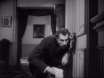 Movie still from “The Song of Bernadette” (1943), directed by Henry King – A black and white photo of a man leaning against a wall; Medium shot, Low angle