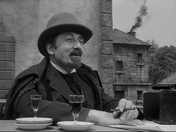 Movie still from “The Song of Bernadette” (1943), directed by Henry King – A man sitting at a table with a cigar and two wine goblets in front of him; Medium shot, Low angle