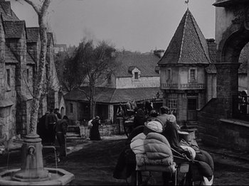 Movie still from “The Song of Bernadette” (1943), directed by Henry King – A black and white photo of people sitting in a courtyard; Wide shot, High angle