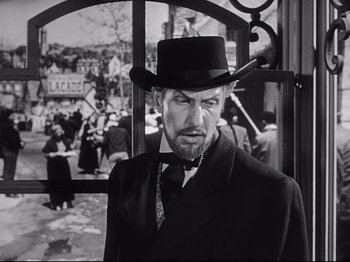 Movie still from “The Song of Bernadette” (1943), directed by Henry King – A black and white photo of a man wearing a top hat; Medium shot, Over the shoulder angle