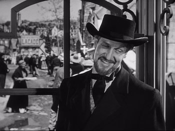 Movie still from “The Song of Bernadette” (1943), directed by Henry King – A black and white photo of a man wearing a suit and a hat; Close Up shot, Over the shoulder angle