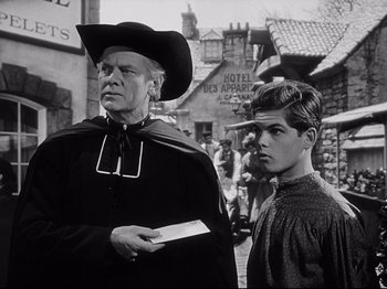 Movie still from “The Song of Bernadette” (1943), directed by Henry King – A man and a young boy standing next to each other on a street; Medium shot, Over the shoulder angle