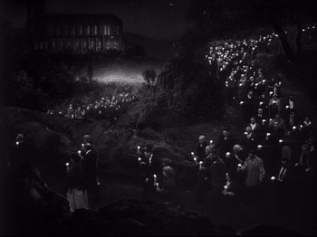 Movie still from “The Song of Bernadette” (1943), directed by Henry King – A group of people holding candles in the dark near a building; Extreme Wide shot, High angle
