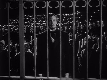 Movie still from “The Song of Bernadette” (1943), directed by Henry King – A black and white photo of a man behind bars; Medium shot, Low angle